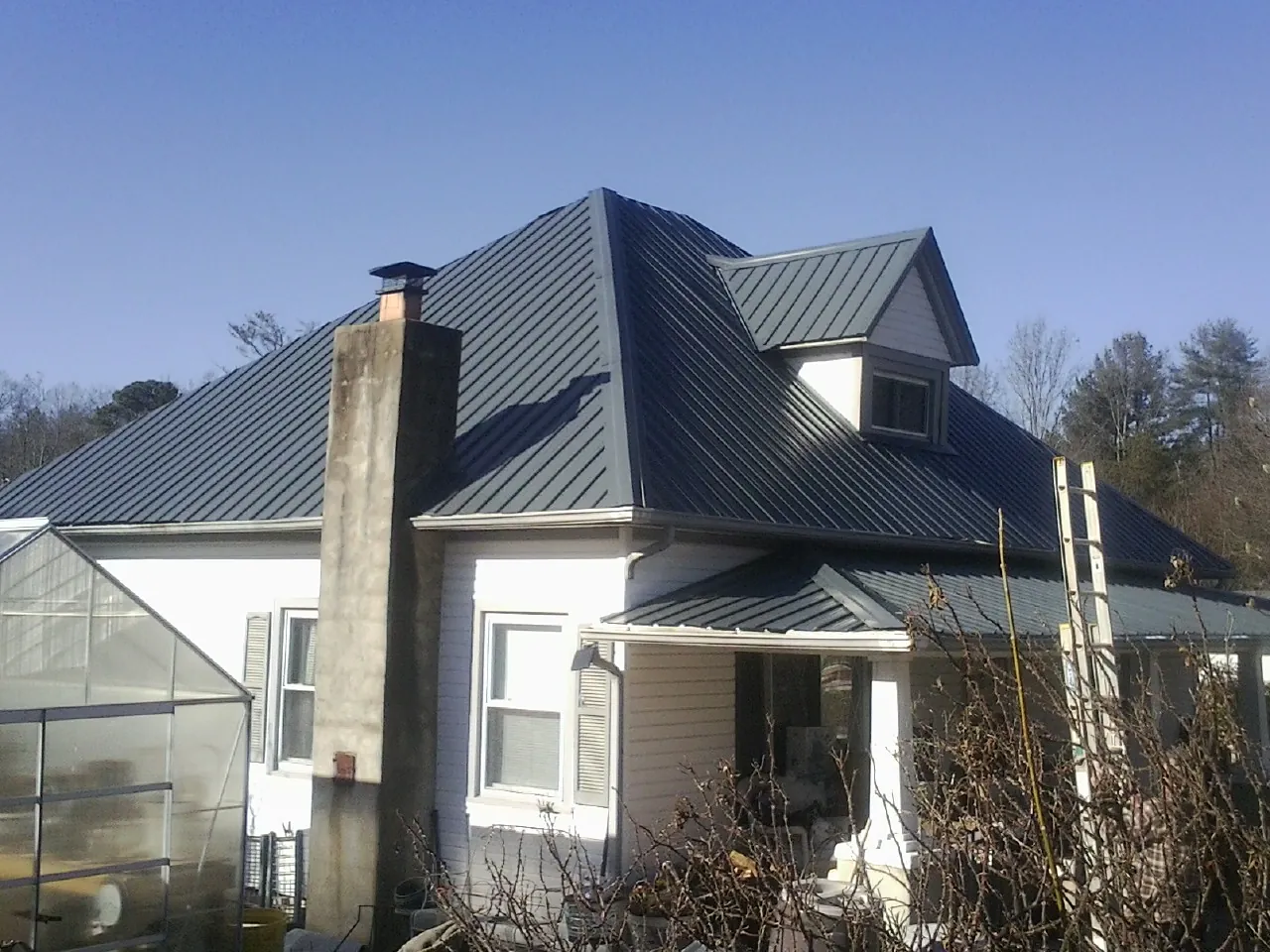 Dark blue standing seam metal roof on a white farmhouse with dormer — Slate & Tile Roof Repair by Roofing Brothers in Prattsburgh