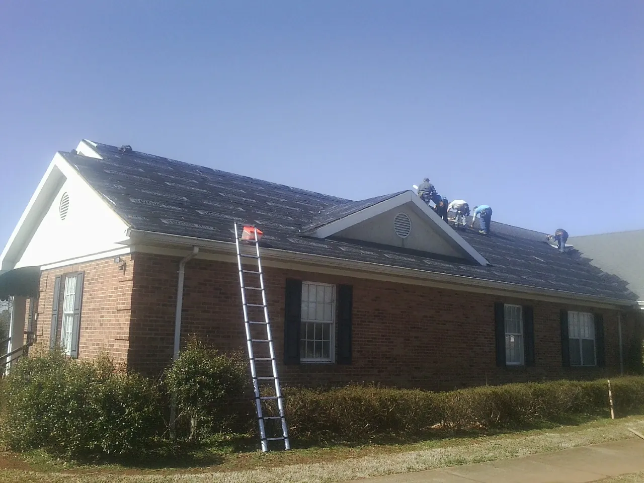 Crew tearing shingles off a brick ranch roof with a ladder set — Metal Roof Repair work by our crew in Prattsburgh