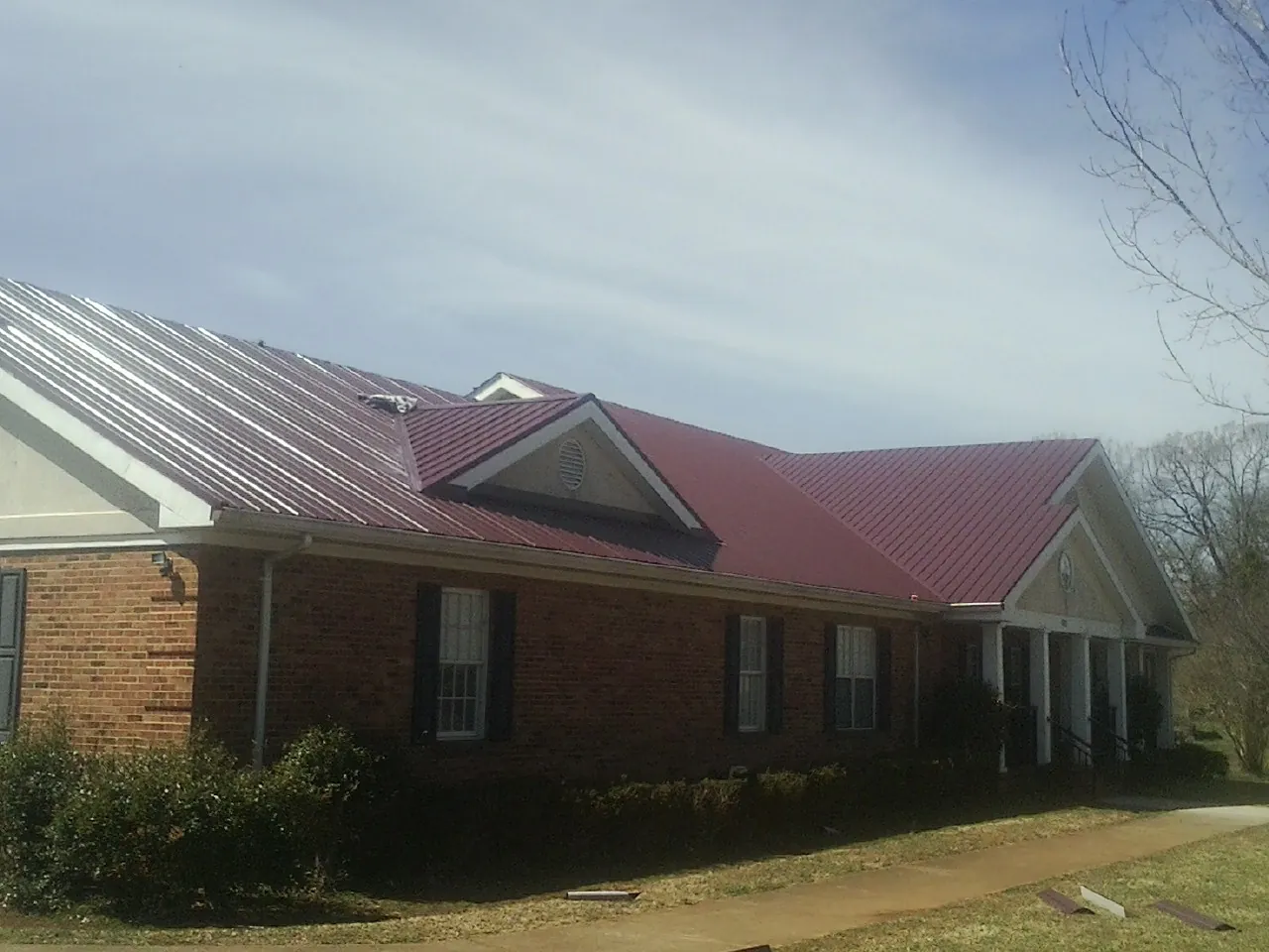 Red metal roof with gabled entries on a long brick building, from a Hail Damage Roof Repair job in Prattsburgh