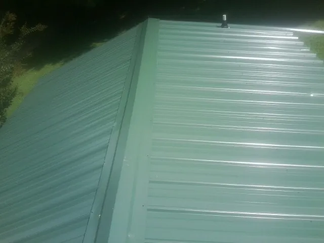 New green metal panels meeting at the ridge of a roof — Flat Roof Repair work by our crew in Prattsburgh