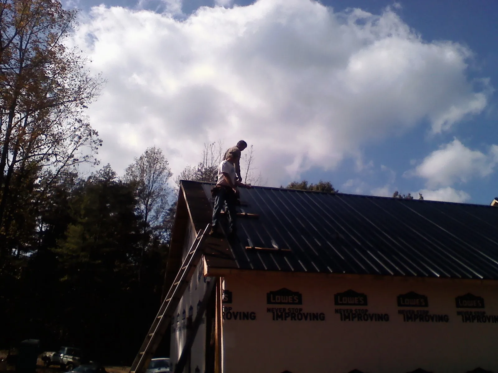 Roofer fastening dark metal panels high against a cloudy sky, from a Roof Inspection job in Prattsburgh